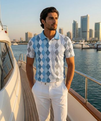 A male model wearing the short-sleeve Almaaz argyle polo shirt and white trousers, standing on a yacht with a sunny marina background.