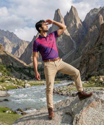 Male model wearing the front of the Parallax sublimated polo shirt while posing in a scenic mountainous landscape with a river.