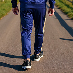 Back view of man walking in navy blue track pants with gold stripes