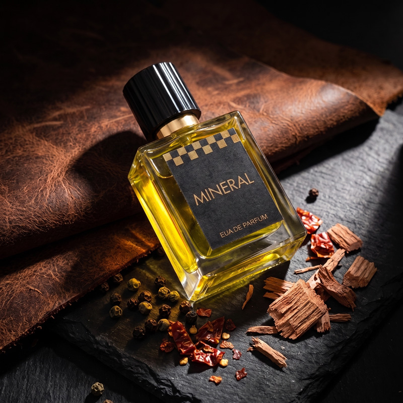 Mineral leather perfume bottle resting on black slate and brown leather, surrounded by raw spices, black peppercorns, and cedarwood shavings.