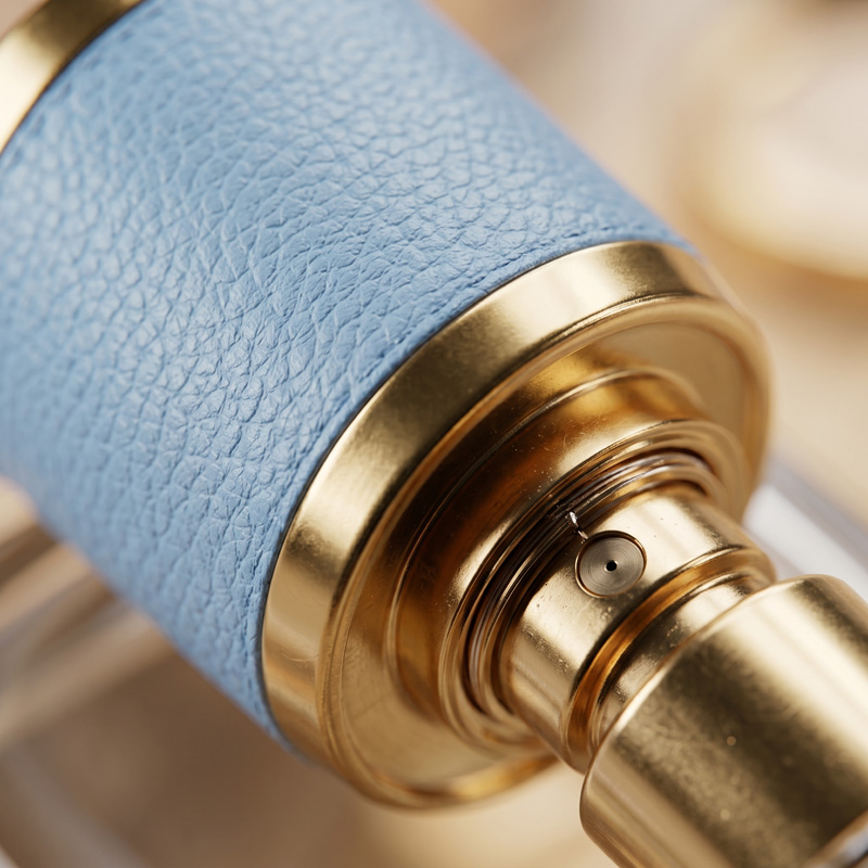 Extreme macro close-up of the gold atomizer spray nozzle and light blue leather-textured cap of the Office Hours perfume bottle.