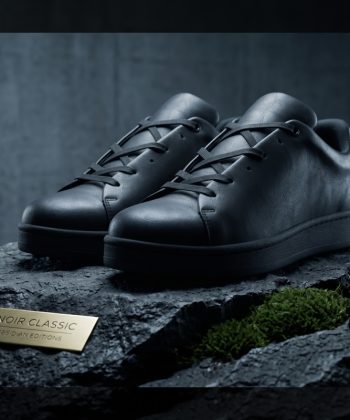 Three-quarter angled view of the Noir Classic Leather Sneakers resting on a textured stone display