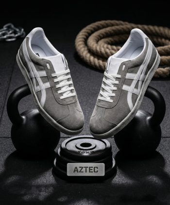 Aztec grey suede athletic sneakers with white stripes balancing on a black kettlebell in a gym