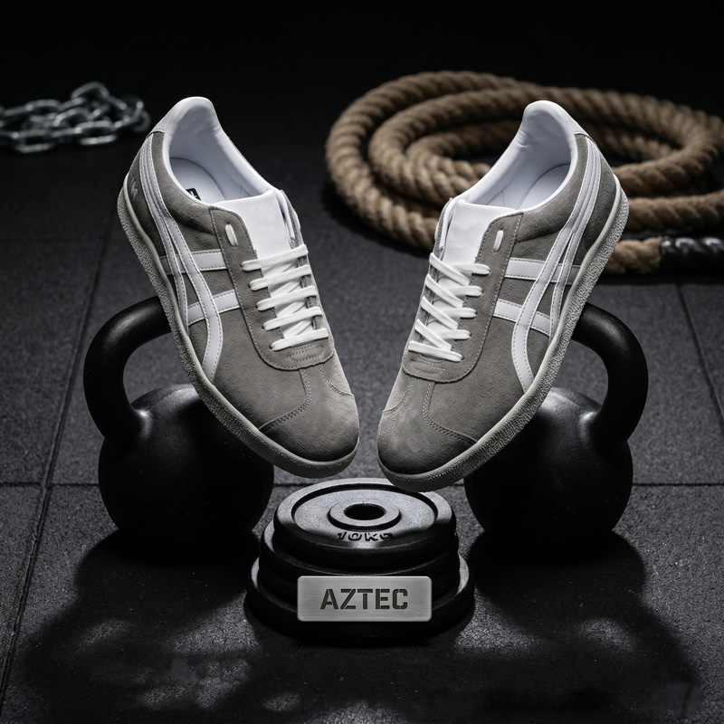Aztec grey suede athletic sneakers with white stripes balancing on a black kettlebell in a gym