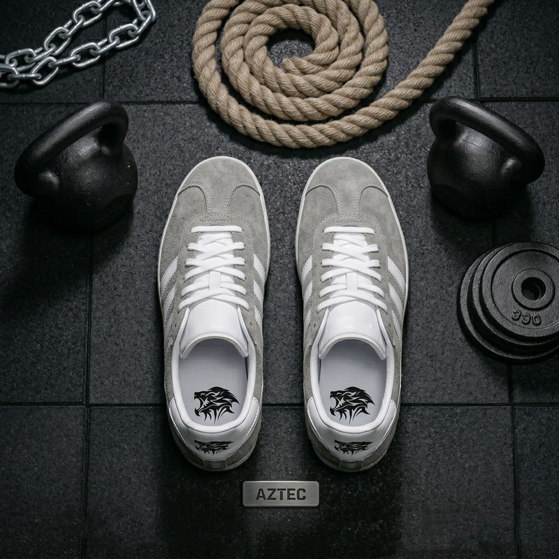Top-down view of Aztec grey suede athletic shoes positioned on a gym floor between kettlebells