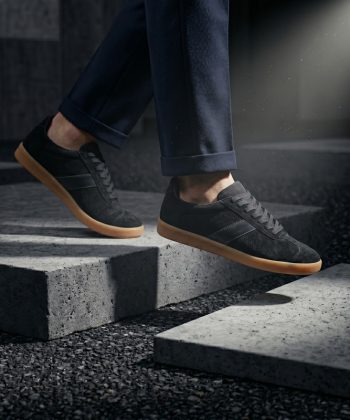A person walking down concrete stairs wearing Asphalt black suede sneakers with gum soles and dark trousers.
