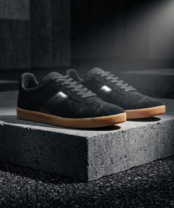 Asphalt black suede sneakers with a gum sole, side profile view resting on a concrete block