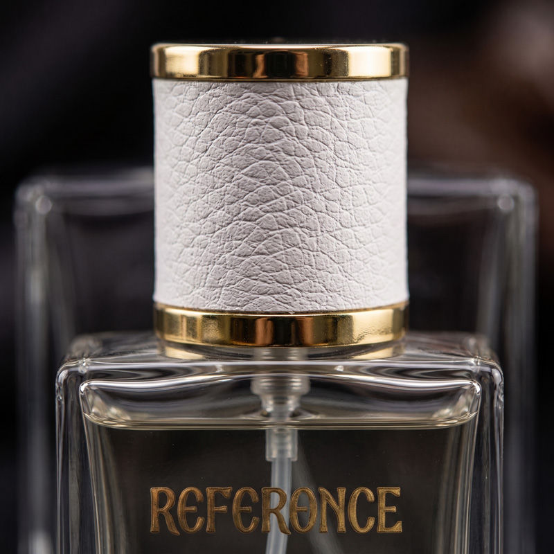 Close-up of the Reference perfume bottle, highlighting the white leather-textured cap with a gold rim and the bold gold lettering on the clear glass.