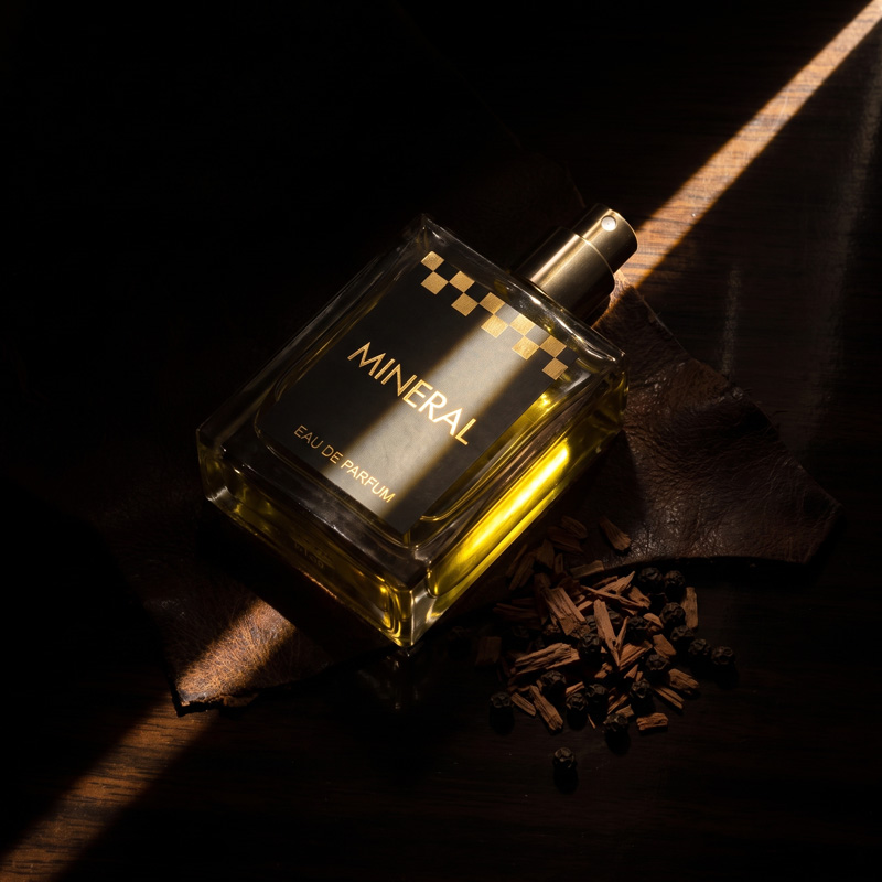 Mineral men's perfume bottle illuminated by a dramatic ray of light on a dark background with wood shavings and black peppercorns